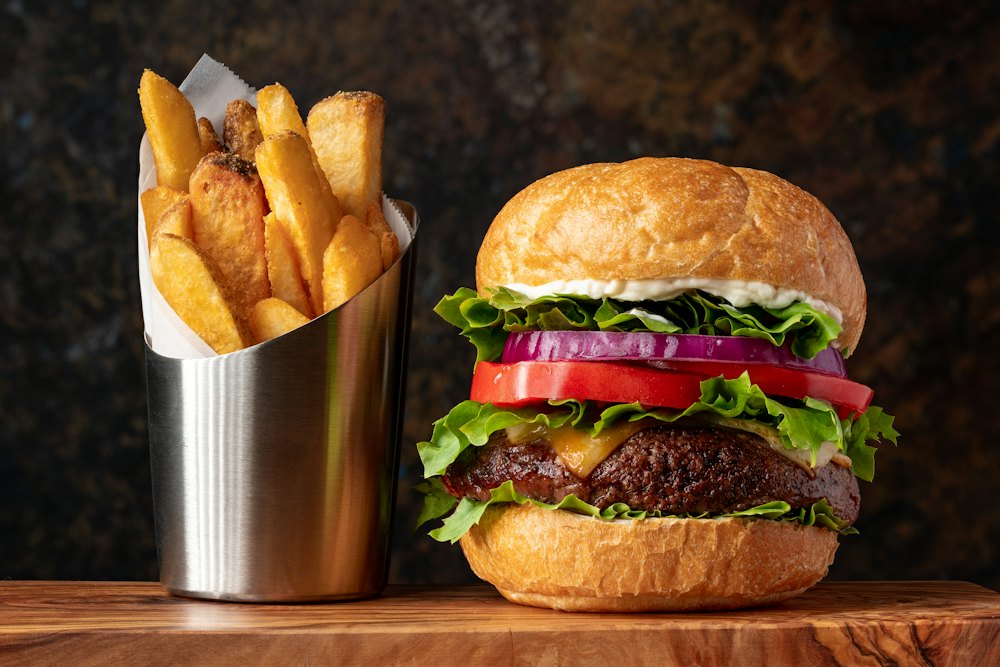 Burger dengan selada, tomat, dan bawang merah di samping kentang goreng