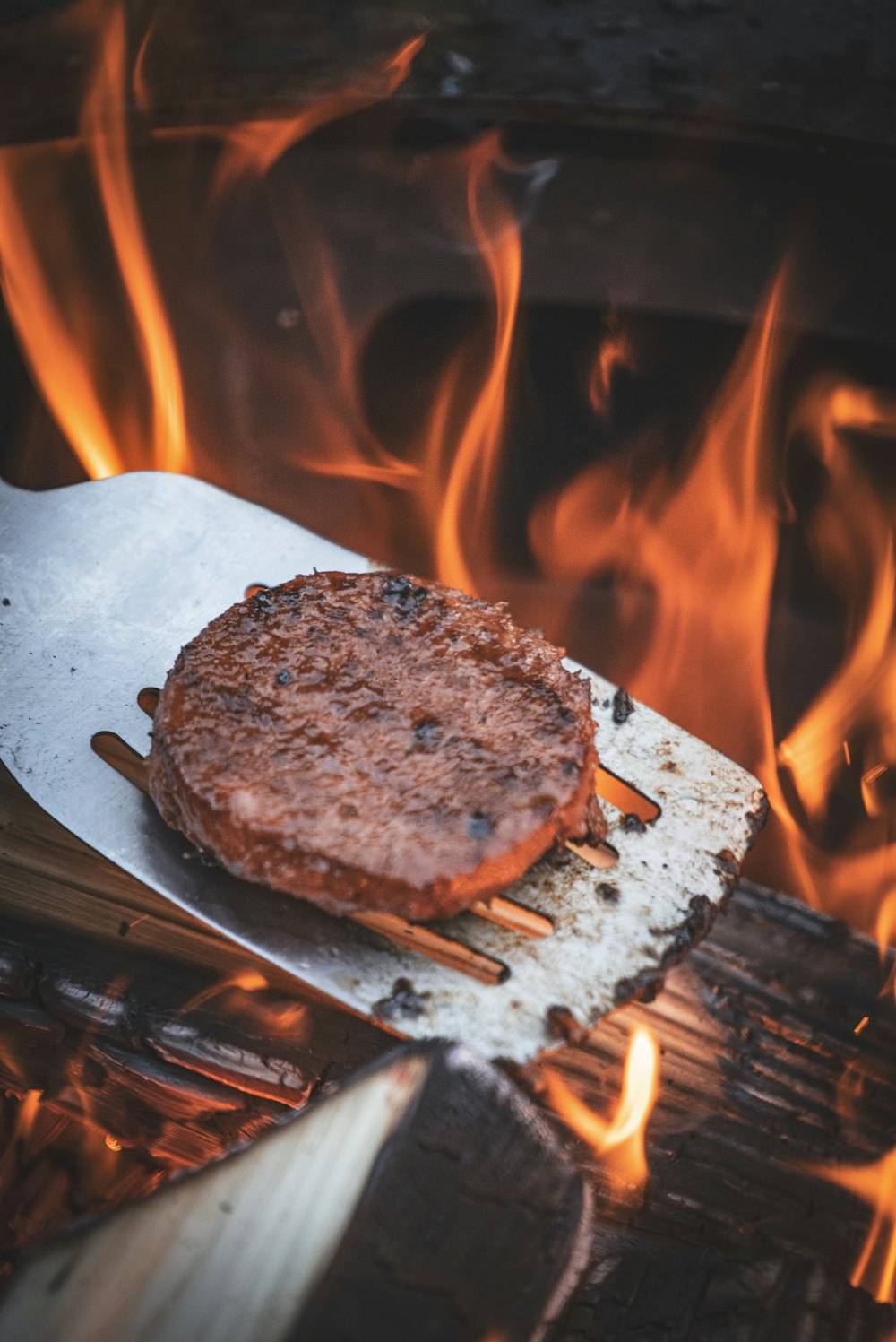 Patty burger di atas spatula dengan api di belakangnya