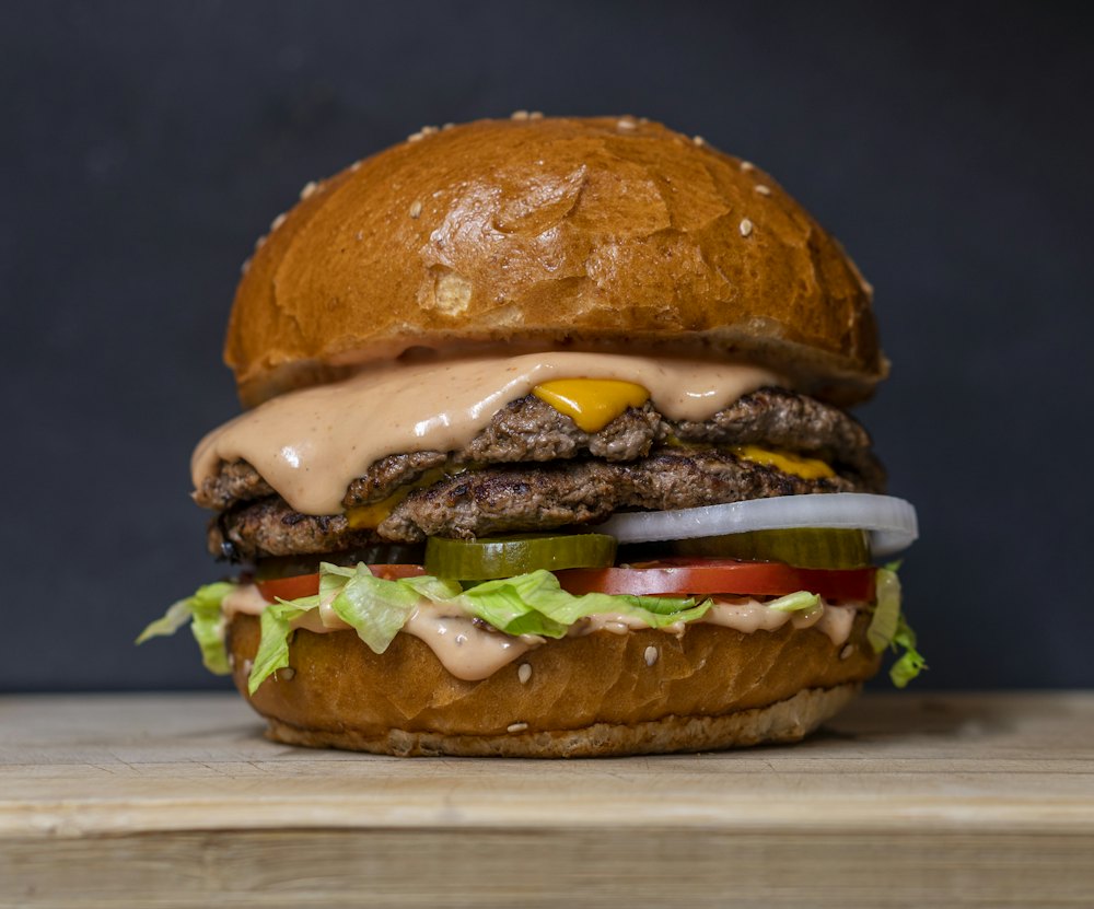 Burger dengan dua patty daging, keju leleh, saus, acar, tomat, dan selada